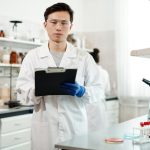Pesquisador de jaleco e óculos de proteção analisa dados em um laboratório moderno.
