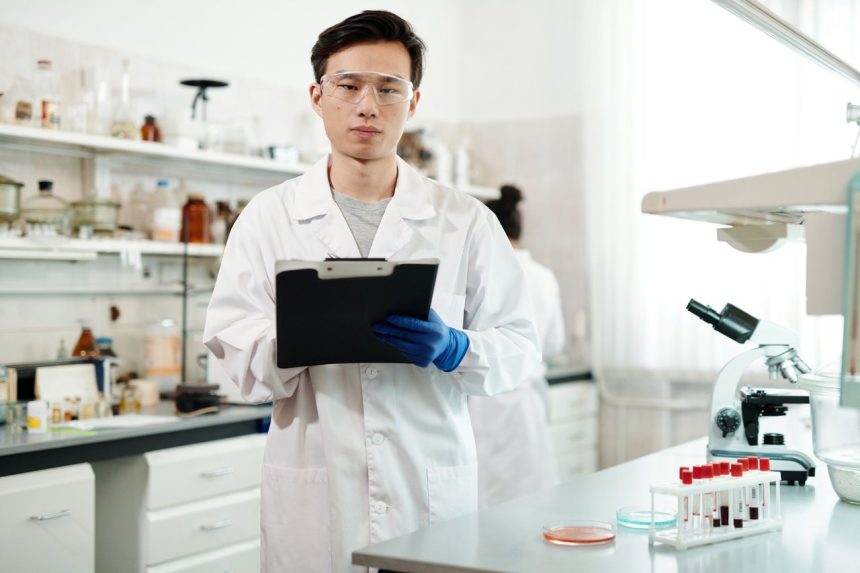 Pesquisador de jaleco e óculos de proteção analisa dados em um laboratório moderno.