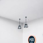 Interior minimalista de um espaço modular com luminárias geométricas e uma placa com a palavra “POD”.
